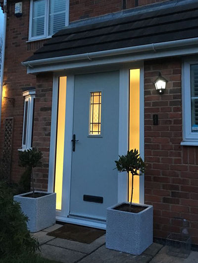 Light coloured composite front door with twin side panels at night