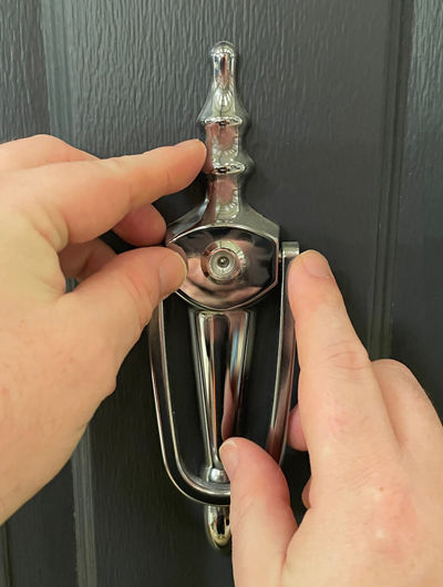 Hands positioning a slim urn knocker with spyhole on a door