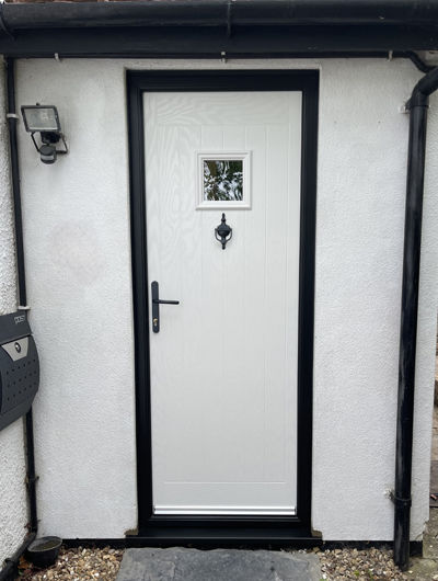White composite door with black frame and hardware on a white house with black surround