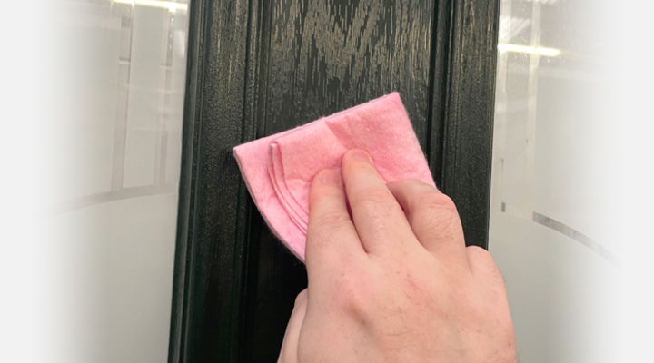 Hand wiping a dark green composite door with a pink cloth